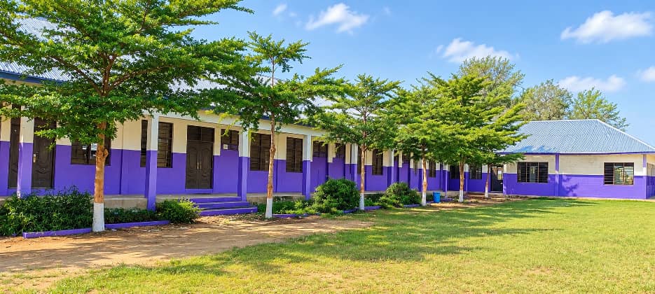 Single-storey classroom row lined with shade trees and a grass lawn